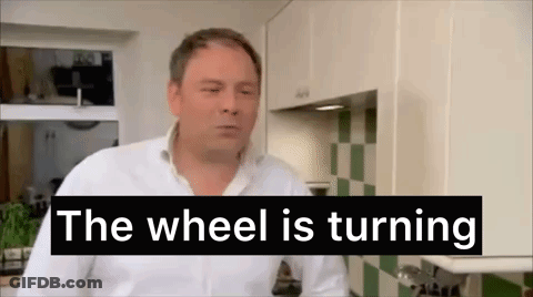 A Man In A Kitchen With The Words `` The Wheel Is Turning '' Behind Him . GIF
