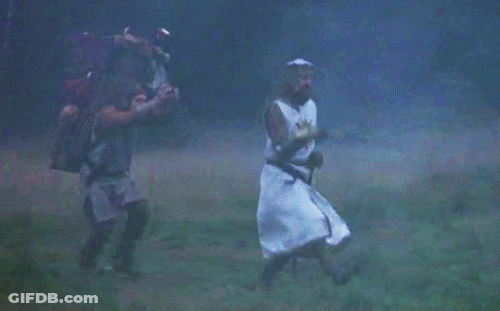 A Man In A Knight 'S Costume Is Walking Through A Field With Another Man Carrying A Backpack . GIF