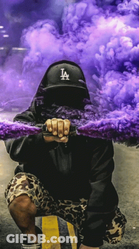 A Man In A La Hat Holds A Purple Smoke Bomb GIF