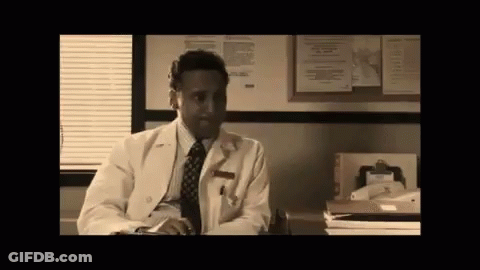 Man In Lab Coat And Tie At Desk In Front Of Bulletin Board GIF