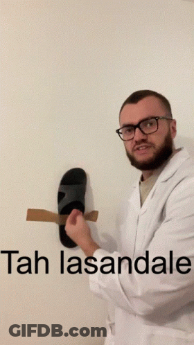 A Man In A Lab Coat Is Holding A Pair Of Sandals In Front Of A Wall That Says Tah Lasantale GIF