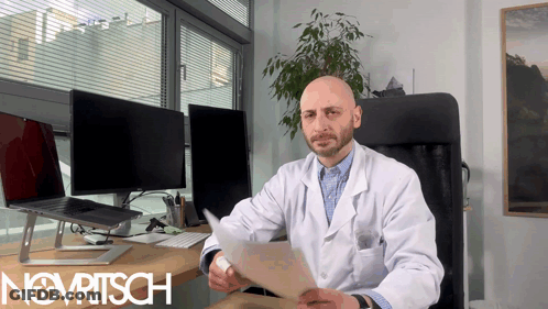A Man In A Lab Coat Is Sitting At A Desk With The Word Novritsch On The Bottom Right GIF