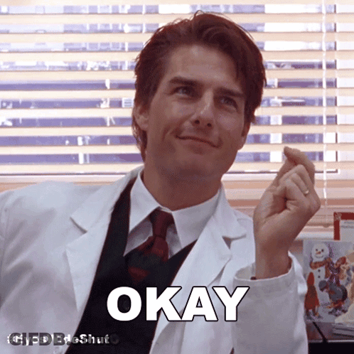 A Man In A Lab Coat Says Okay In Front Of Blinds GIF