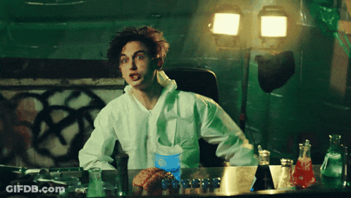 A Man In A Lab Coat Sits At A Desk With A Blue Cup That Says ' Coca Cola ' On It GIF