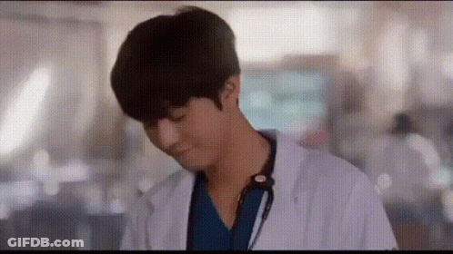 A Man In A Lab Coat With A Stethoscope Around His Neck Is Standing In A Hallway . GIF