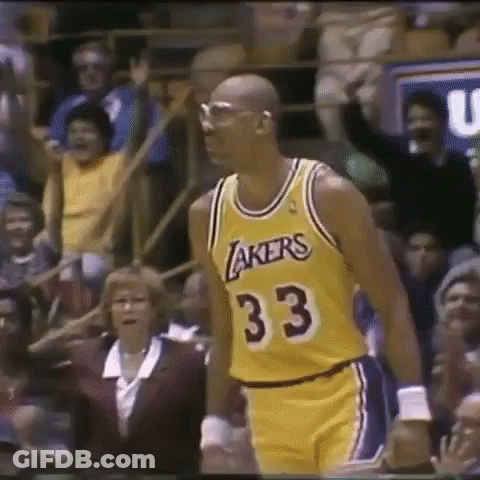 A Man In A Lakers Jersey Is Standing In Front Of A Crowd Of People . GIF