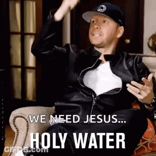 A Man In A Leather Jacket And Hat Is Sitting On A Couch And Saying We Need Jesus ... Holy Water . GIF