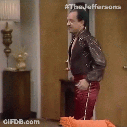 A Man In A Leather Jacket And Red Pants Is Standing In A Room . GIF