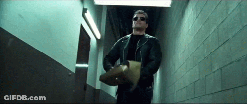 A Man In A Leather Jacket And Sunglasses Is Walking Down A Hallway Holding A Piece Of Paper . GIF