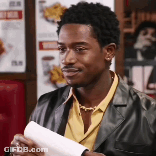A Man In A Leather Jacket And Yellow Shirt Is Holding A Piece Of Paper GIF