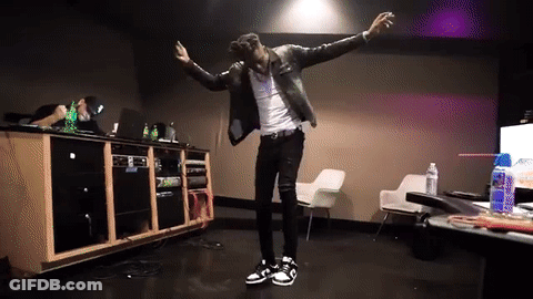 A Man In A Leather Jacket Is Dancing In A Room With A Table And Chairs GIF