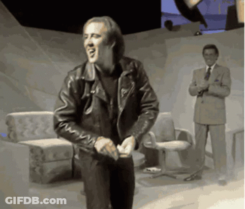 A Man In A Leather Jacket Is Dancing In Front Of A Man In A Suit And Tie GIF