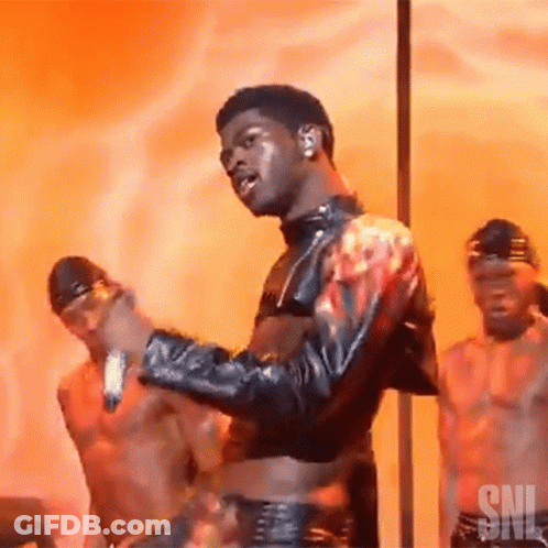 A Man In A Leather Jacket Is Dancing On A Pole With Two Men Behind Him . GIF