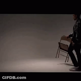 A Man In A Leather Jacket Is Holding A Folding Chair In His Hand . GIF