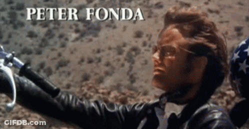A Man In A Leather Jacket Is Holding A Motorcycle Handlebars And The Name Peter Fonda Is Visible Above Him GIF