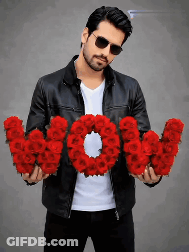 A Man In A Leather Jacket Is Holding A Wreath Of Red Roses That Spell Out The Word Wow GIF