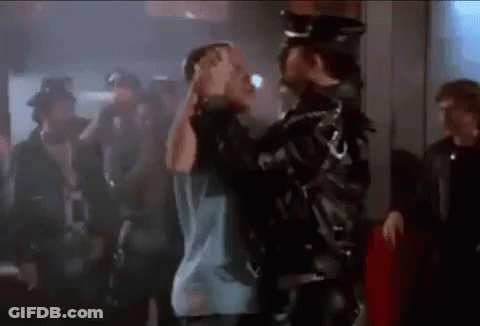 A Man In A Leather Jacket Is Holding Another Man 'S Head In A Crowd Of People . GIF