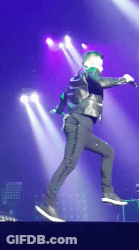 A Man In A Leather Jacket Is Jumping In The Air With A Microphone GIF