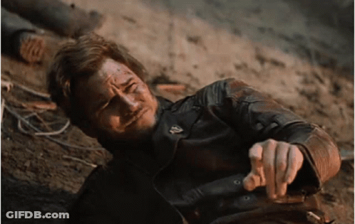 A Man In A Leather Jacket Is Laying On The Ground Pointing At The Camera GIF