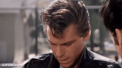 A Man In A Leather Jacket Is Looking Down At Something While Another Man Looks On . GIF