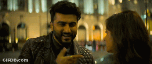 A Man In A Leather Jacket Is Pointing At A Woman 'S Face GIF