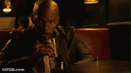 A Man In A Leather Jacket Is Sitting At A Table Drinking A Drink . GIF