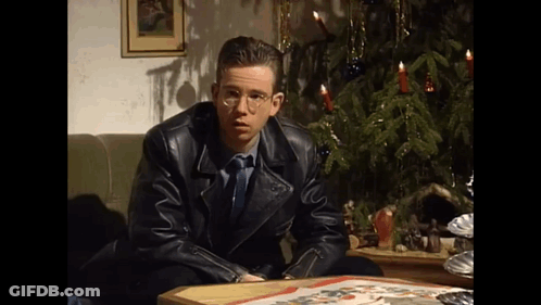 A Man In A Leather Jacket Is Sitting At A Table In Front Of A Christmas Tree . GIF