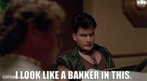 A Man In A Leather Jacket Is Sitting At A Table Reading A Book And Says `` I Look Like A Banker In This '' GIF