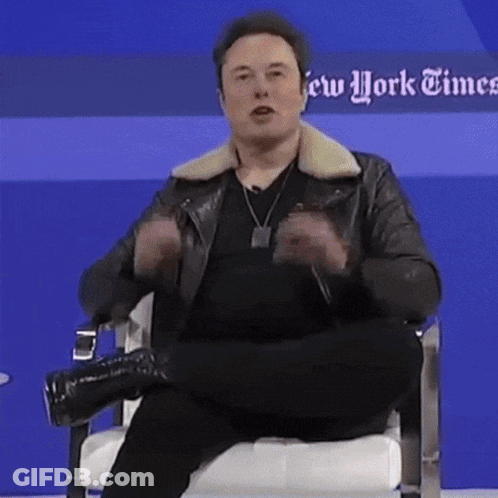 A Man In A Leather Jacket Is Sitting In A Chair In Front Of A Blue Wall That Says New York Times GIF