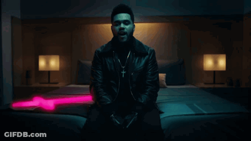 A Man In A Leather Jacket Is Sitting On A Bed In A Dark Room GIF