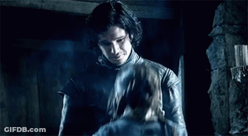 A Man In A Leather Jacket Is Standing In A Dark Room Holding A Sword . GIF