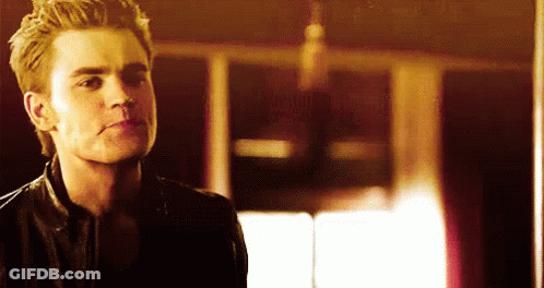 A Man In A Leather Jacket Is Standing In A Dark Room Looking At The Camera . GIF