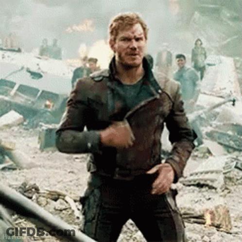 A Man In A Leather Jacket Is Standing In A Destroyed City Holding A Knife . GIF
