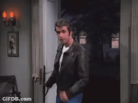 A Man In A Leather Jacket Is Standing In A Doorway Holding A Gun . GIF