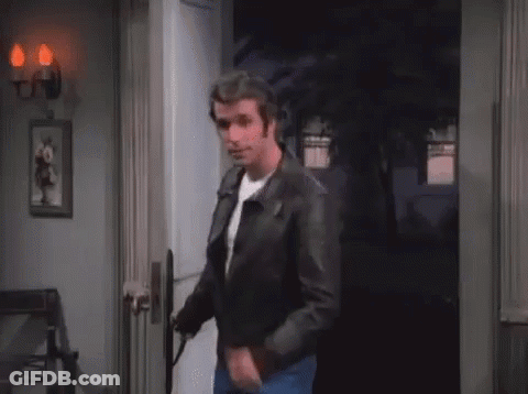A Man In A Leather Jacket Is Standing In A Doorway With The Letter A Written On His Chest . GIF