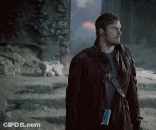 A Man In A Leather Jacket Is Standing In Front Of A Building In A Dark Room . GIF