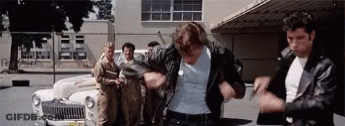 A Man In A Leather Jacket Is Standing In Front Of A Car . GIF