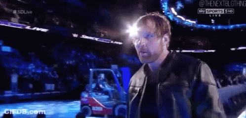 A Man In A Leather Jacket Is Standing In Front Of A Crowd At A Wrestling Event . GIF