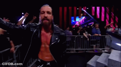 A Man In A Leather Jacket Is Standing In Front Of A Crowd Of People . GIF