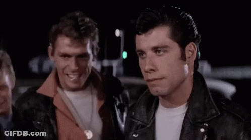 A Man In A Leather Jacket Is Standing In Front Of A Group Of Men In A Parking Lot . GIF