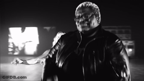 A Man In A Leather Jacket Is Standing In Front Of A Large M GIF