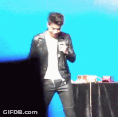 A Man In A Leather Jacket Is Standing In Front Of A Microphone GIF