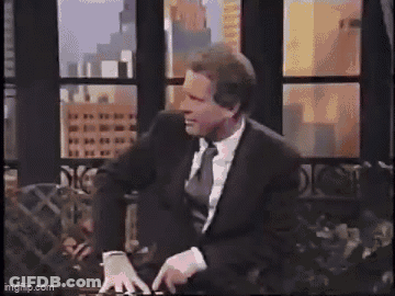 A Man In A Leather Jacket Is Standing In Front Of A Window In A Living Room . GIF