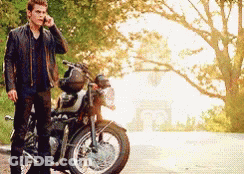 A Man In A Leather Jacket Is Standing Next To A Motorcycle Talking On A Cell Phone GIF