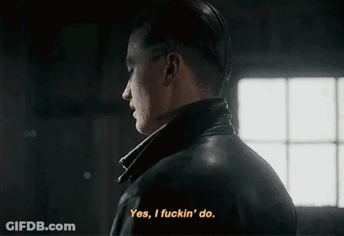 A Man In A Leather Jacket Is Talking To Another Man In A Dark Room . GIF
