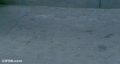 A Man In A Leather Jacket Is Walking Down A Narrow Street GIF