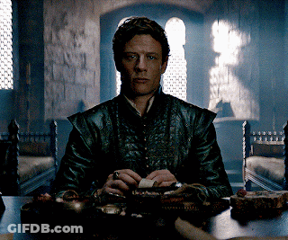 A Man In A Leather Jacket Sits At A Table Holding A Piece Of Paper GIF