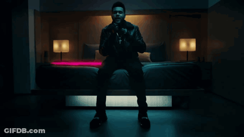 A Man In A Leather Jacket Sits On A Bed GIF