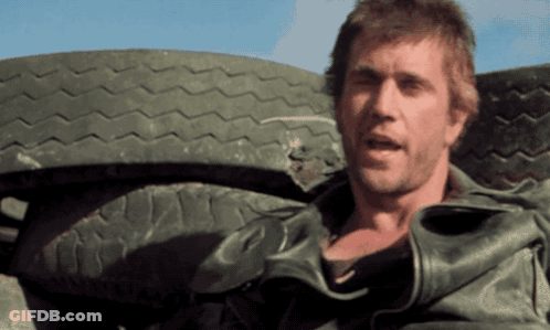 A Man In A Leather Jacket Stands In Front Of A Large Tire GIF