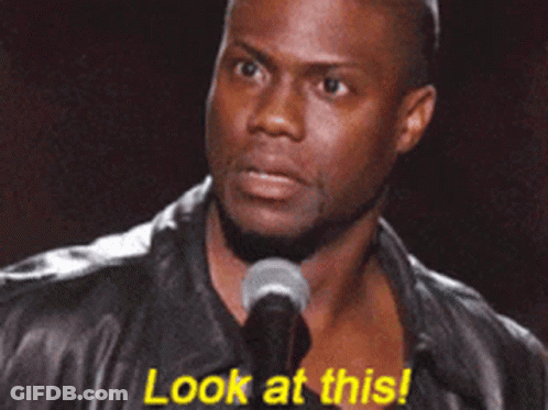 A Man In A Leather Jacket Stands In Front Of A Microphone And Says " Look At This " GIF